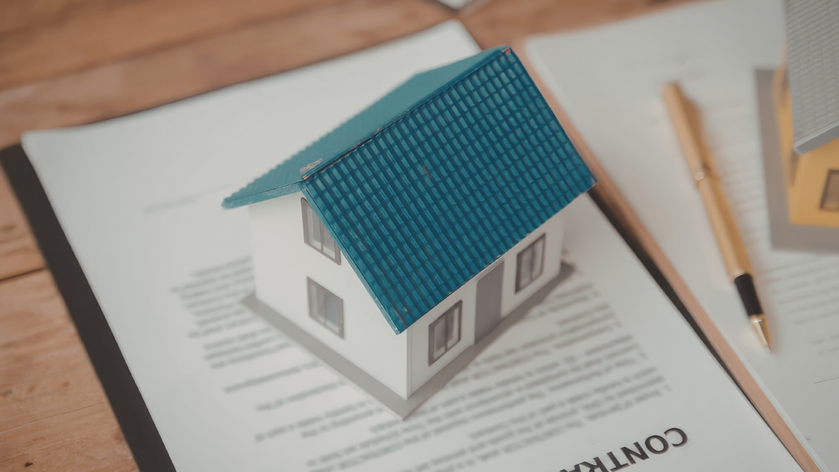 Small house model placed on top of documents with a pen, representing property ownership or real estate planning.