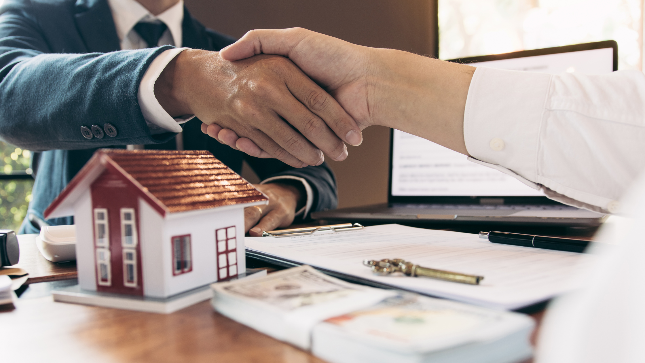 Property investor and client shaking hands across a table with a model home, representing real estate investment opportunities, property market activity, and investment consultation services in Australia.
