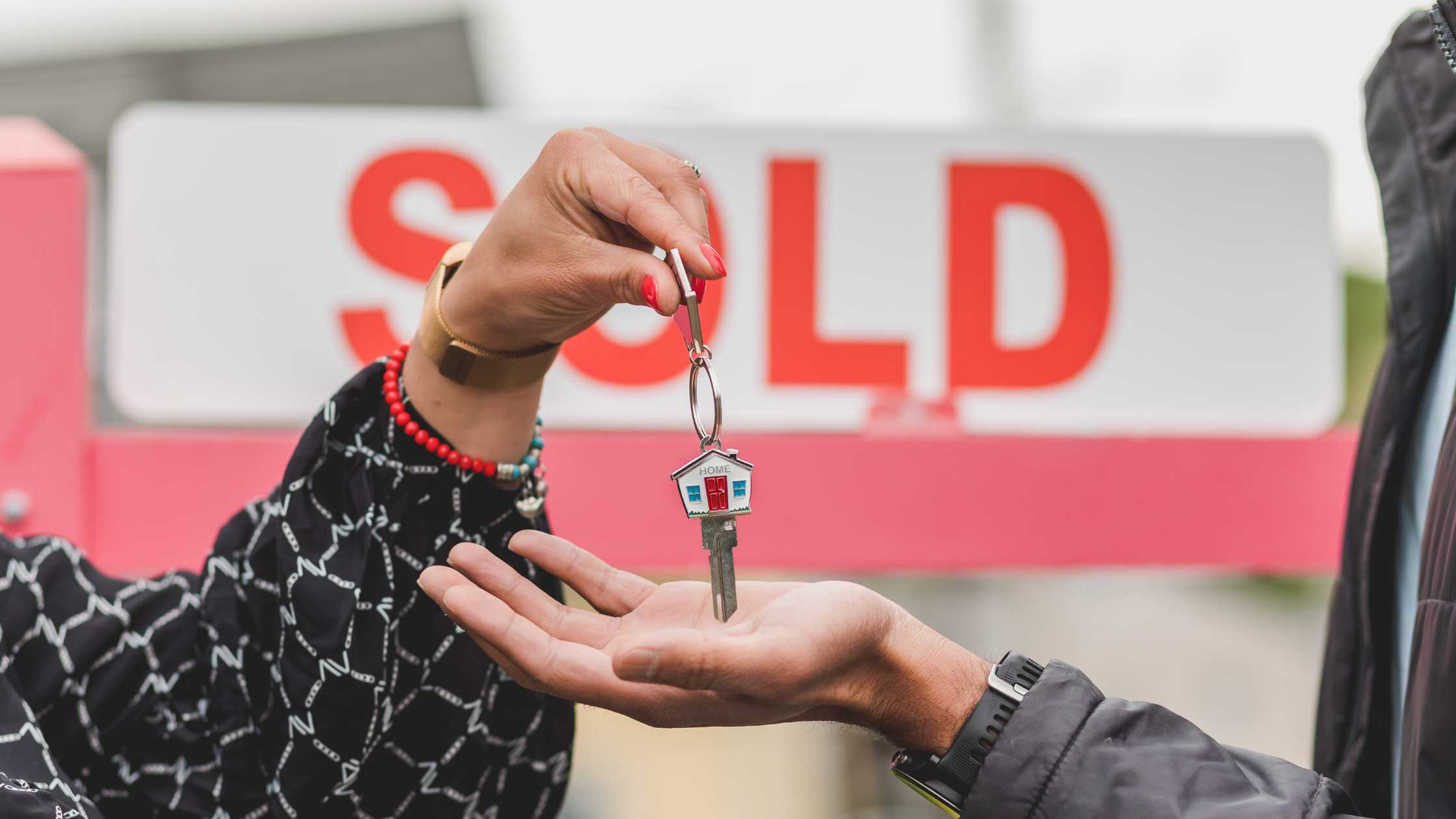 **Alt Text:** Person handing over house keys in front of a sold property sign, representing home buying, buyer confidence, property transactions, and activity in the Australian real estate market.
