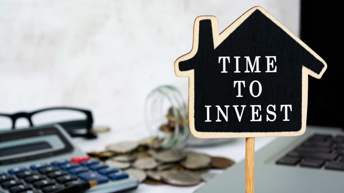 Person holding a "Time to Invest" sign above a calculator and financial documents, symbolising strategic property investment, wealth building, and making informed real estate investment decisions in Australia.