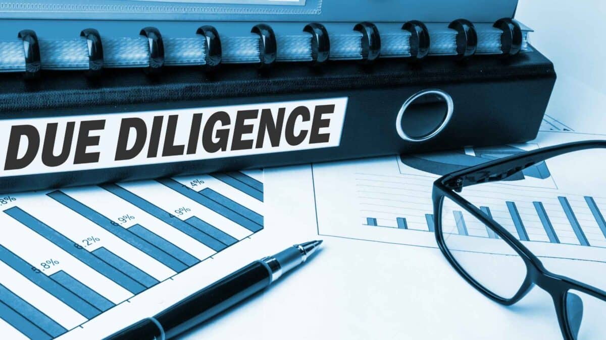 Due diligence concept with a binder labeled “DUE DILIGENCE,” financial charts, pen and eyeglasses on a desk.