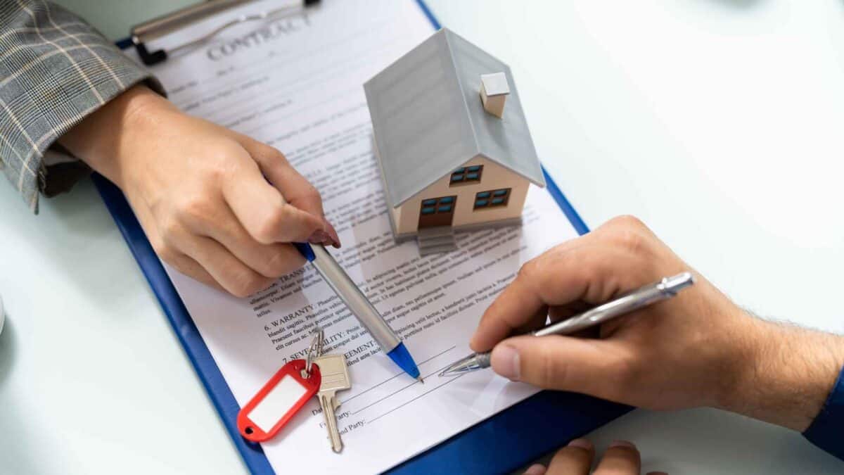 Hands signing a property purchase contract beside a model house and keys, representing the legal process of buying property in Australia.