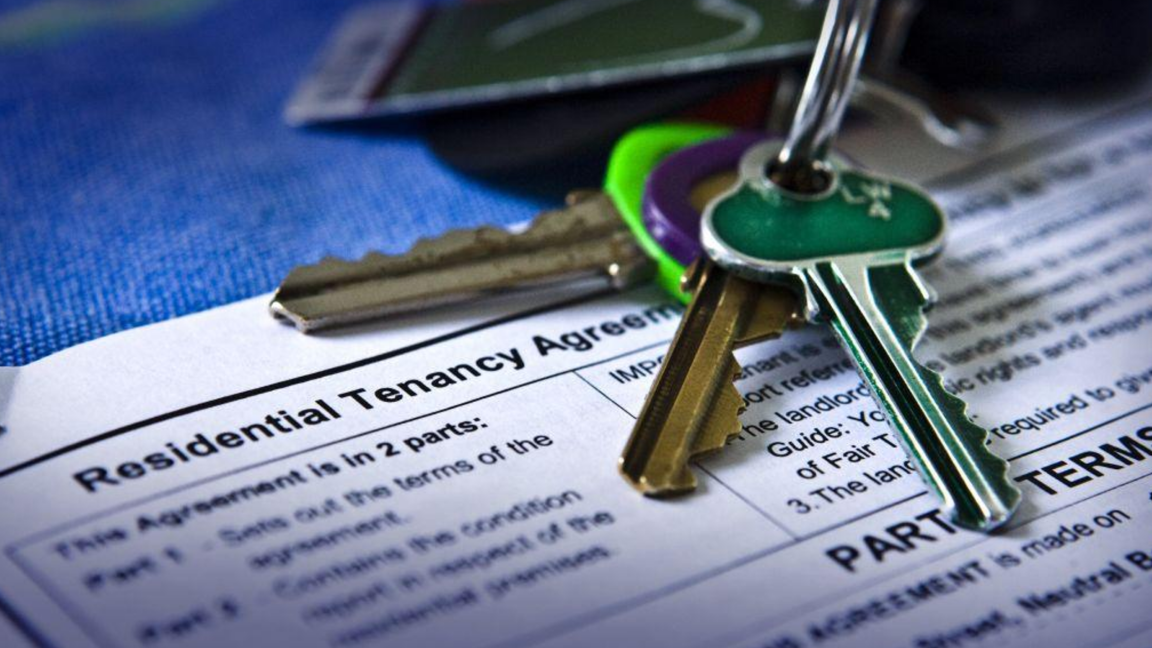 Keys resting on a residential tenancy agreement, representing a rental property purchase and existing tenant lease.